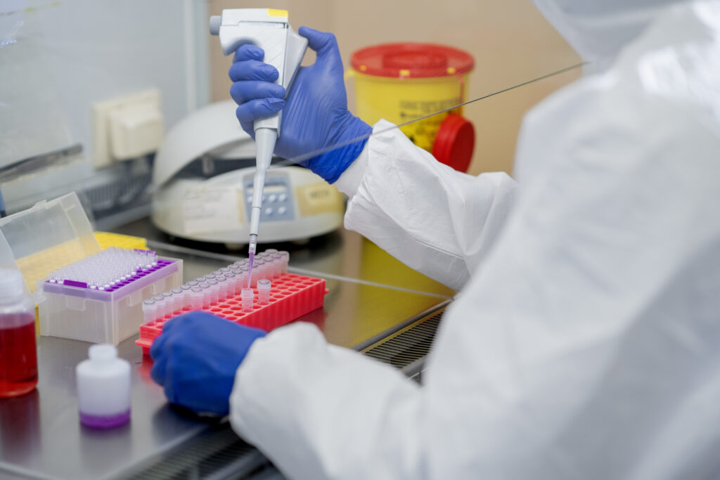 Laboratory technician using a pipette to transfer assay liquid into reaction vials during short-chain peptide bioregulators testing.